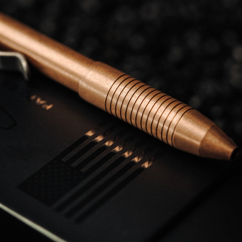 Close-up of bronze EDC pen made in USA with textured grip resting on black surface