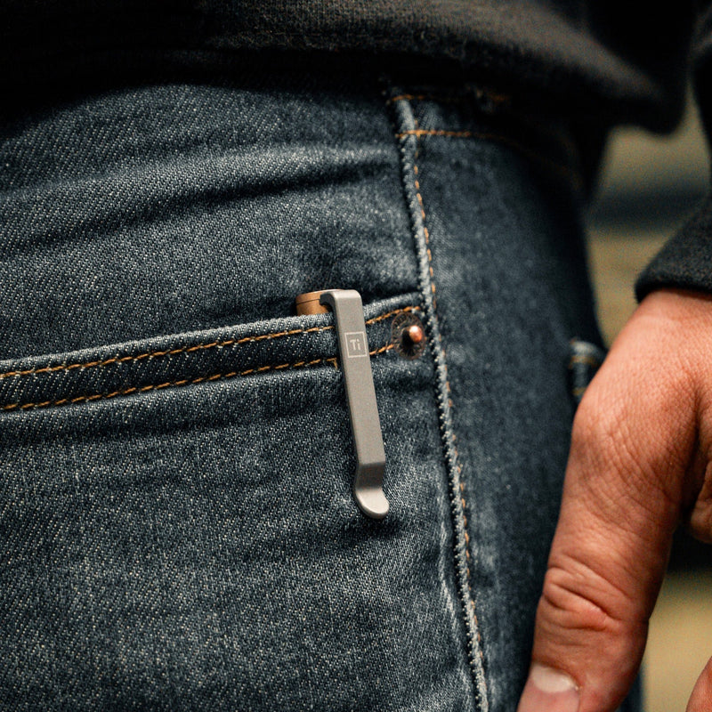 bronze EDC pen made in USA clipped to blue denim jeans pocket with hand nearby