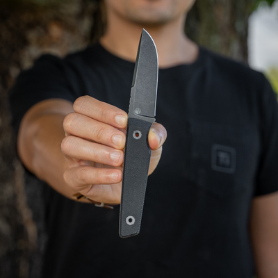 Person holding a black micarta knife with a sleek blade and textured handle outdoors