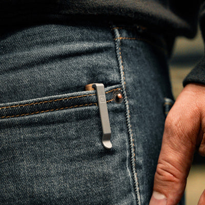 bronze EDC pen made in USA clipped to blue denim jeans pocket with hand nearby