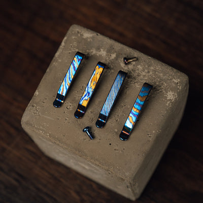 Colorful titanium CNC milled EDC accessories clips displayed on a concrete block