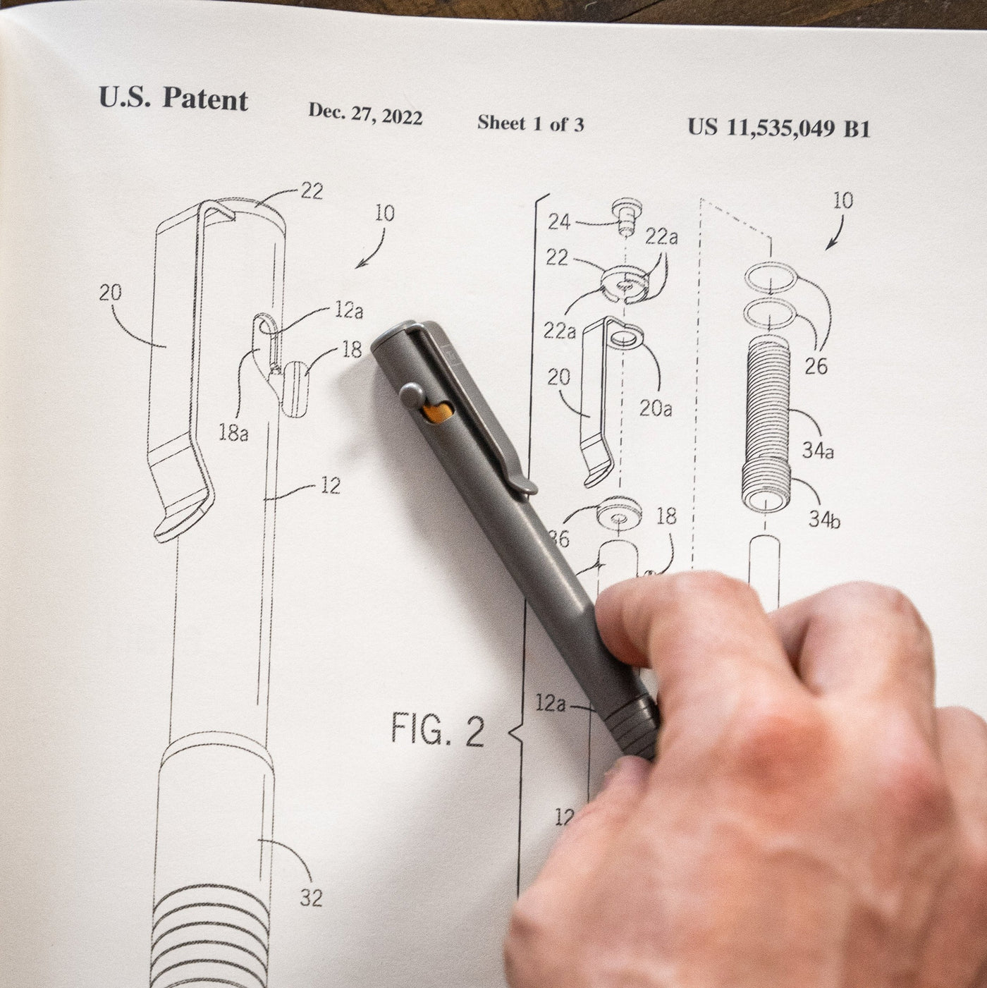 EDC bolt action pen by Big Idea Design LLC held over patent design schematic drawing