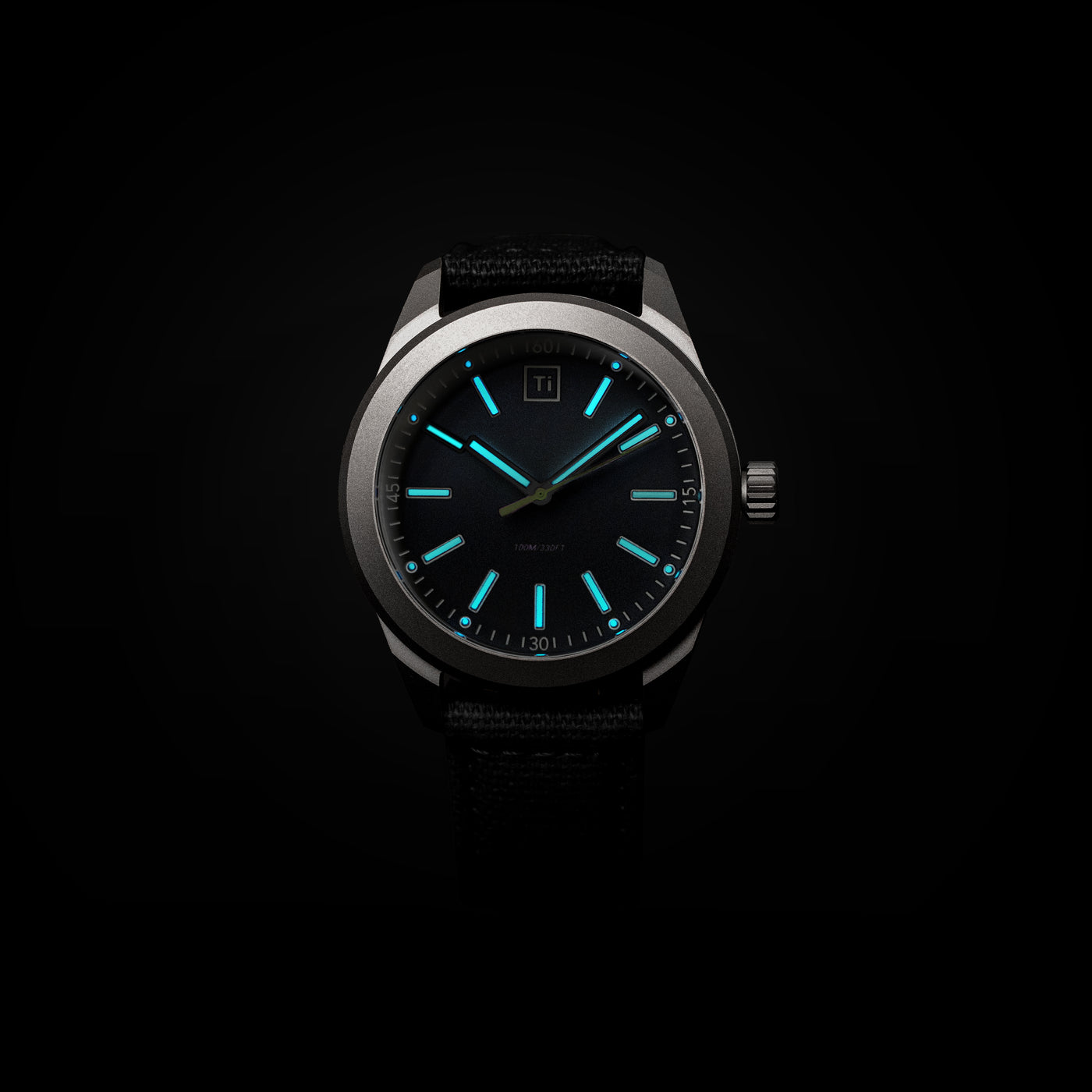 Big Idea Design LLC titanium field watch with luminous blue hands and hour markers on black dial and fabric strap