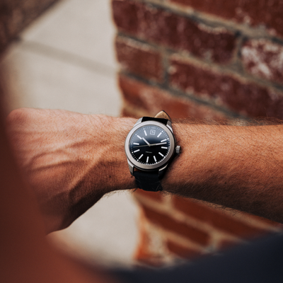Big Idea Design LLC titanium field watch on a male wrist with black dial and leather strap