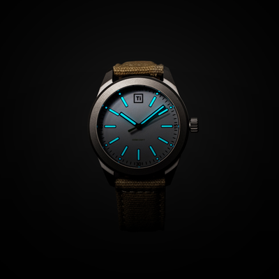 Big Idea Design LLC titanium field watch with luminous blue hands and markers dark dial titanium case canvas strap