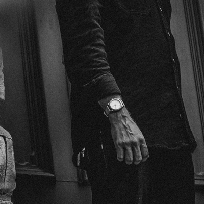 Black and white street photo of a male wrist wearing a Big Idea Design LLC titanium field watch with leather strap