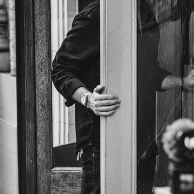 Man wearing Big Idea Design LLC titanium field watch on wrist while opening a glass door in black and white photo