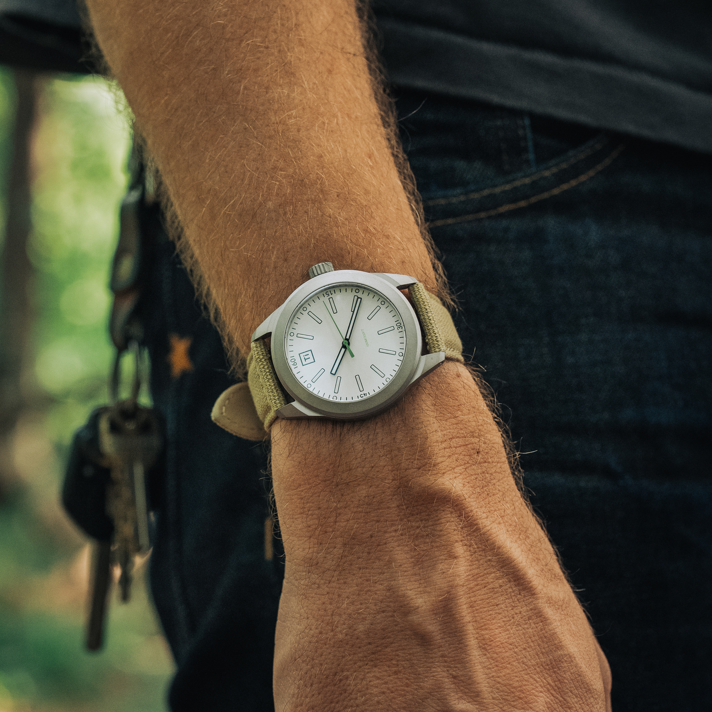 Big Idea Design LLC titanium field watch on a wrist with khaki canvas strap and white dial outdoors