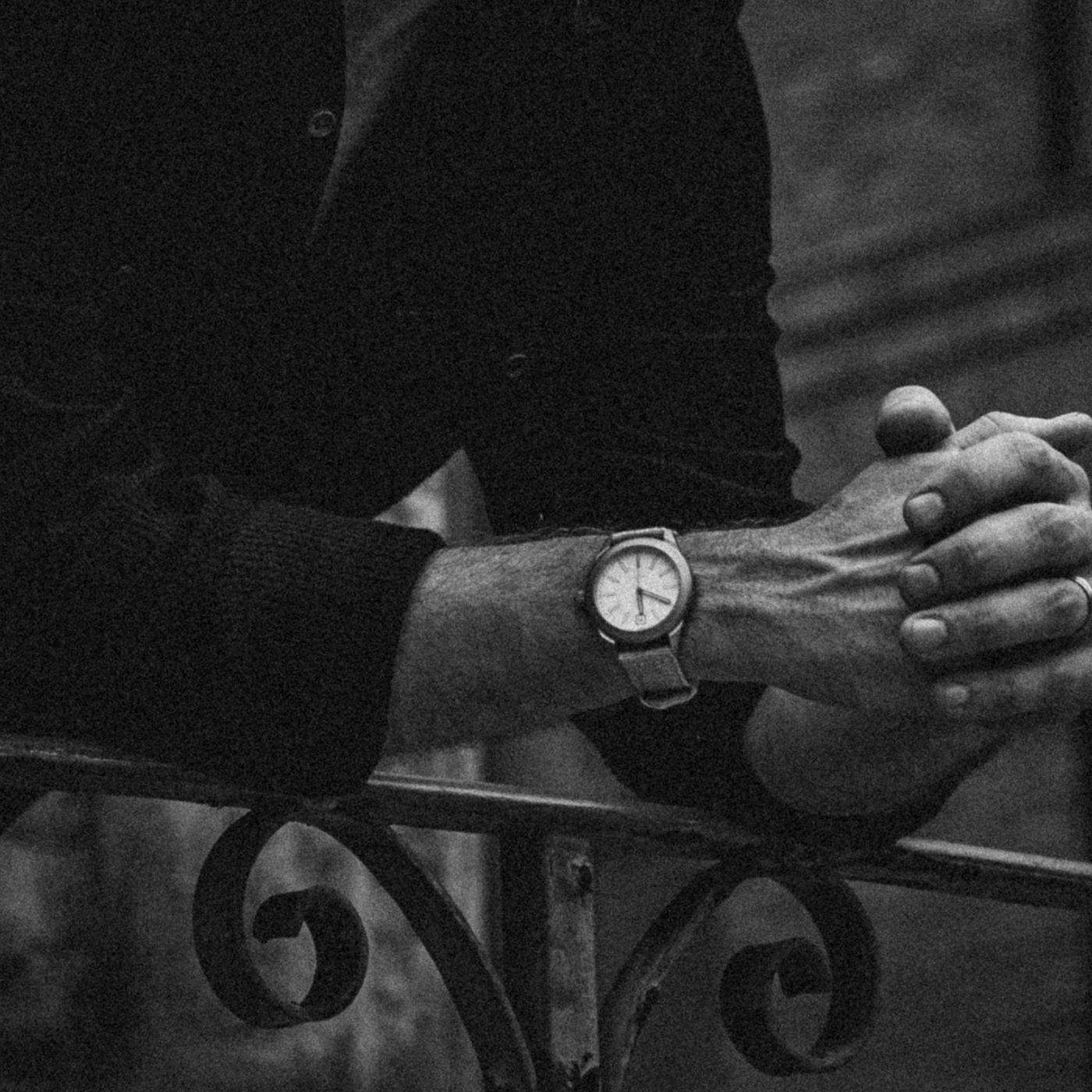 Black and white image of a person leaning on railing wearing Big Idea Design LLC titanium field watch with light dial