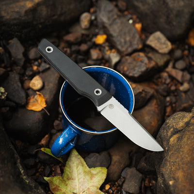 BIGiDESIGN-USA Fixed Blad knife with black handle resting on blue cup outdoors on rocky ground