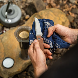 BIGiDESIGN-USA Fixed Blad knife with brown handle being cleaned using a blue cloth outdoors