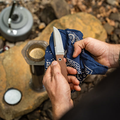 BIGiDESIGN-USA Fixed Blad knife with brown handle being cleaned using a blue cloth outdoors