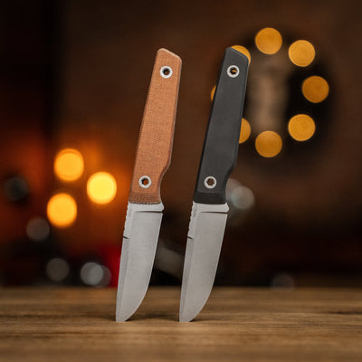 BIGiDESIGN-USA fixed blad knives with brown and black handles standing on wooden surface with blurred warm lights background