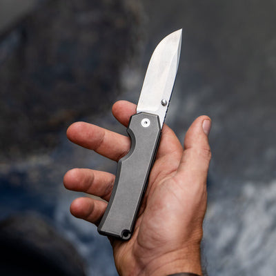 BIG IDEA DESIGN LLC titanium pocket knife with sleek blade held in hand over blurred background