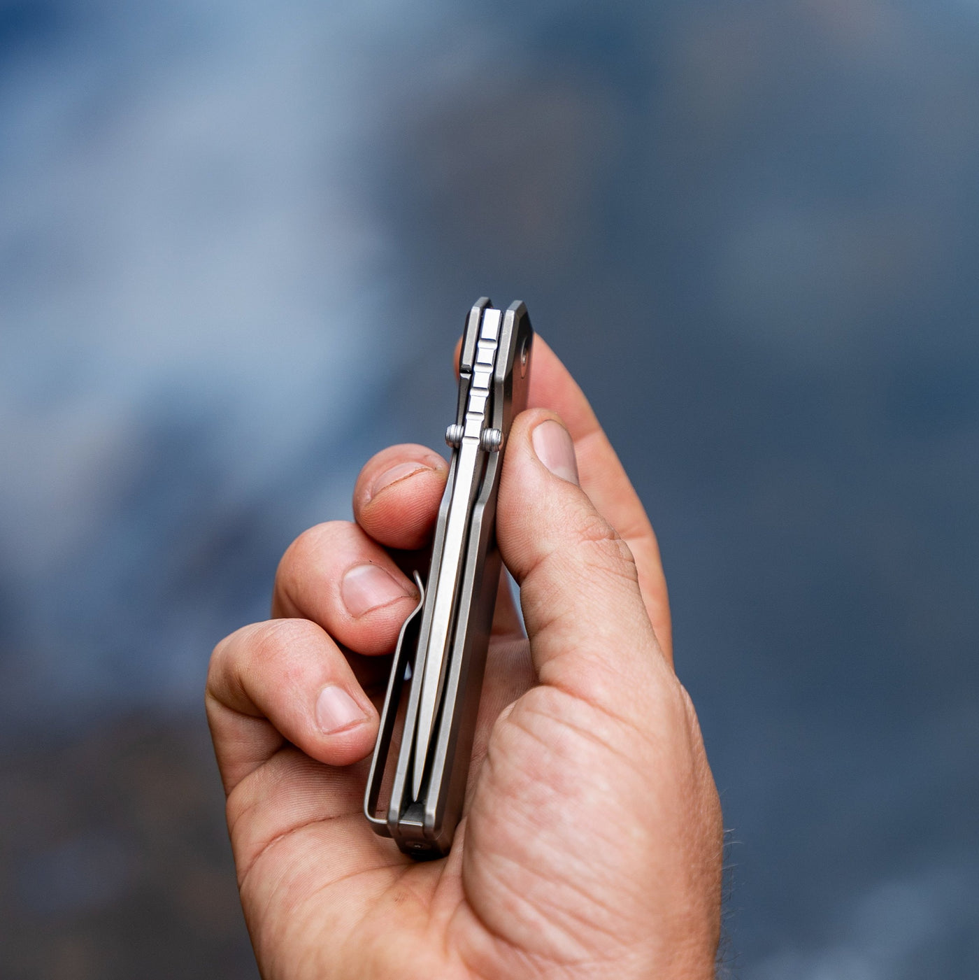 Hand holding a closed titanium pocket knife from BIG IDEA DESIGN LLC with a sleek metal frame