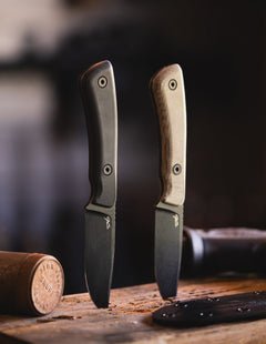 Two JS Deano fixed blade knives with black blades and different handle colors on wooden surface