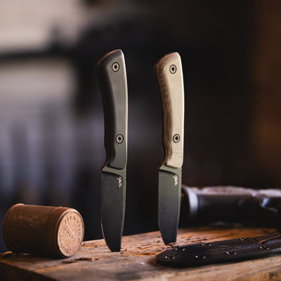 Two JS Deano fixed blade knives with black blades and different handle colors on wooden surface