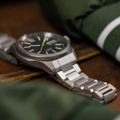 Close-up of a wristwatch with a premium titanium bracelet by BIG IDEA DESIGN LLC on a wooden surface