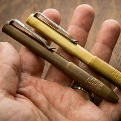 Brass and bronze EDC pens with pocket clips in hand showing compact durable everyday carry design