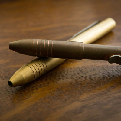 Two brass and bronze metal Pens with grooved grip and pocket clip on a wooden tabletop