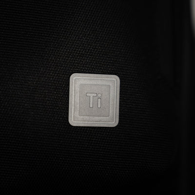 Close-up of Big Idea Design LLC titanium logo on black fabric everyday carry backpack