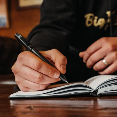 Person writing in notebook using a sleek black titanium capped pen by BIG IDEA DESIGN LLC