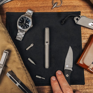 Titanium capped pen from BIG IDEA DESIGN LLC placed on a black cloth with watch, knife, and tools