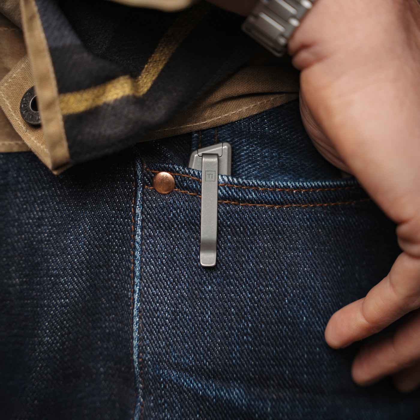 Compact titanium pocket knife clipped on blue denim jeans pocket with hand nearby
