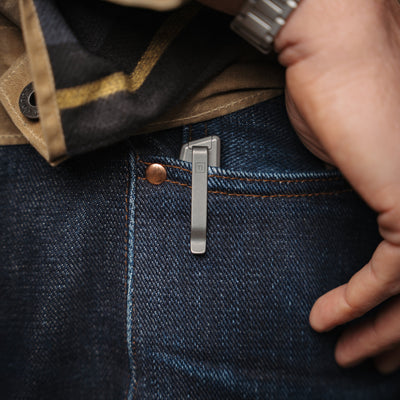 Compact titanium pocket knife clipped on blue denim jeans pocket with hand nearby