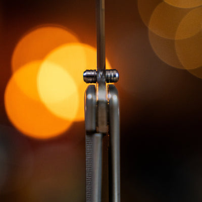 Close-up side view of a titanium pocket knife hinge and blade detail with blurred lights background