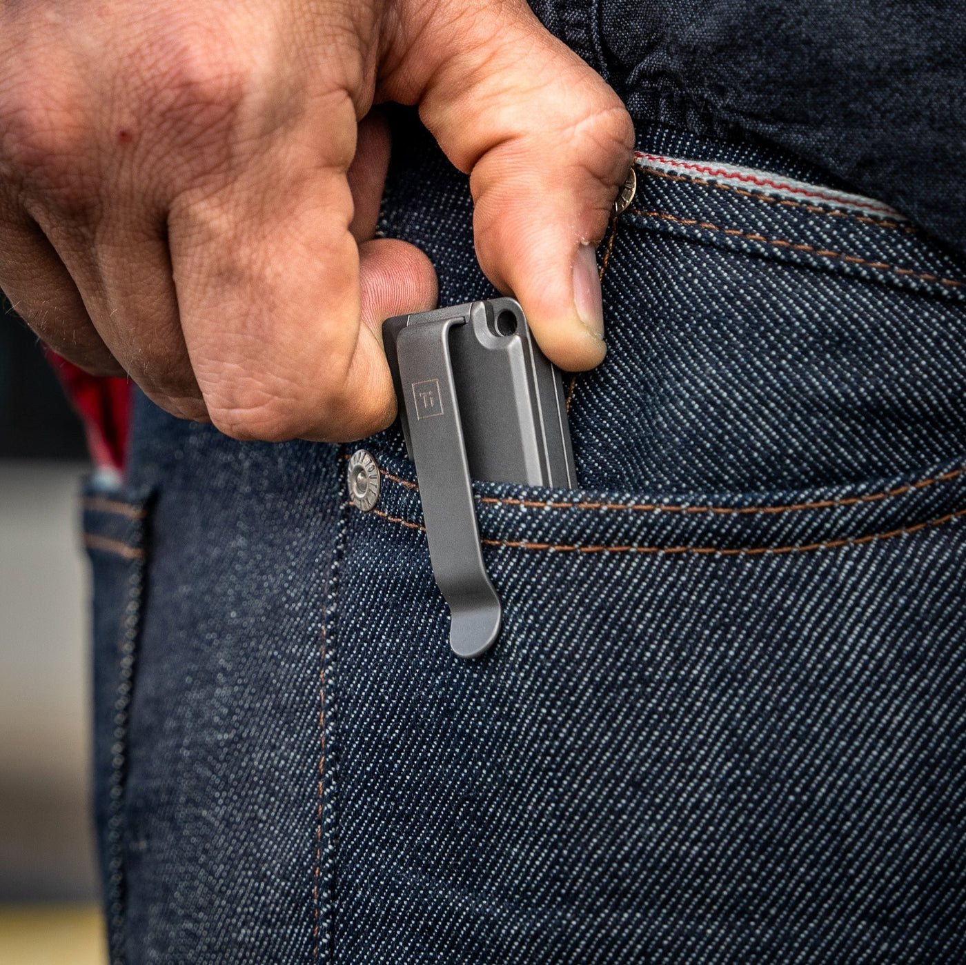 Hand placing a titanium pocket knife with clip into the front pocket of dark blue denim jeans