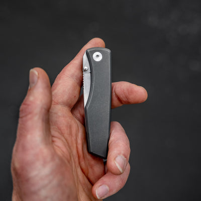Hand holding a closed titanium pocket knife by Big Idea Design LLC with a sleek metal handle