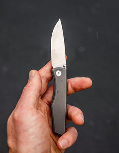 Hand holding an open titanium pocket knife with a sleek metal handle and sharp blade