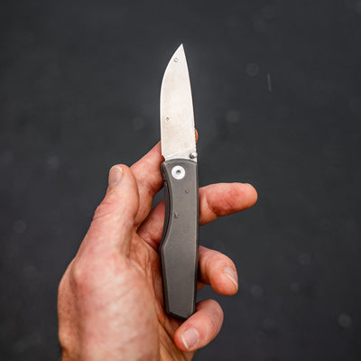 Hand holding an open titanium pocket knife with a sleek metal handle and sharp blade