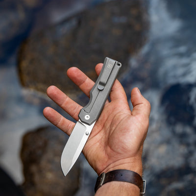 Hand holding BIG IDEA DESIGN LLC titanium pocket knife with sleek gray handle and sharp blade