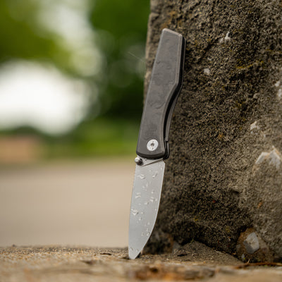 Titanium pocket knife with water droplets standing upright against a rough stone surface outdoors