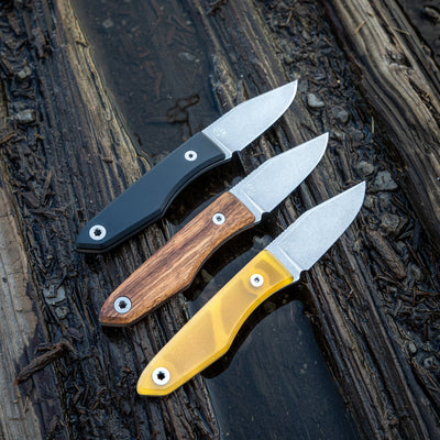Three USA lookout fixed blade knives with black, wood, and yellow handles displayed on weathered wood