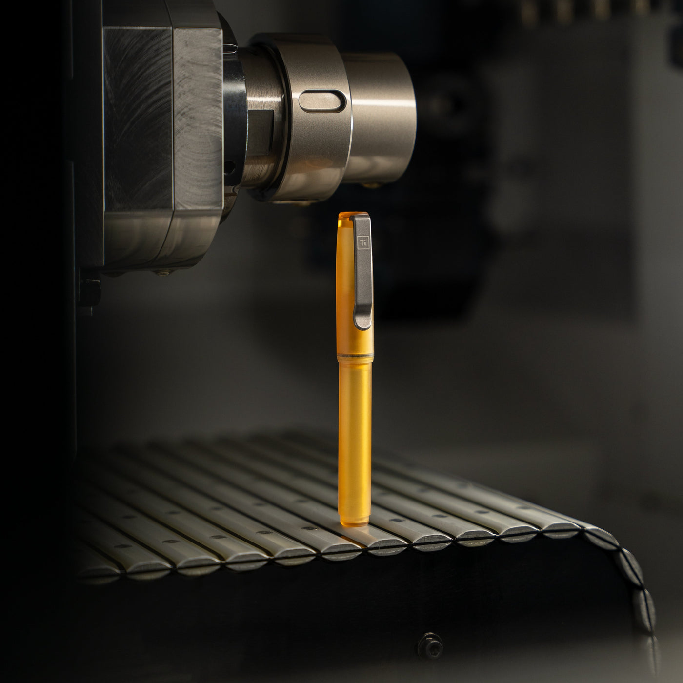BIGiDESIGN-USA yellow USA made EDC pen standing upright on a metal surface near industrial machinery