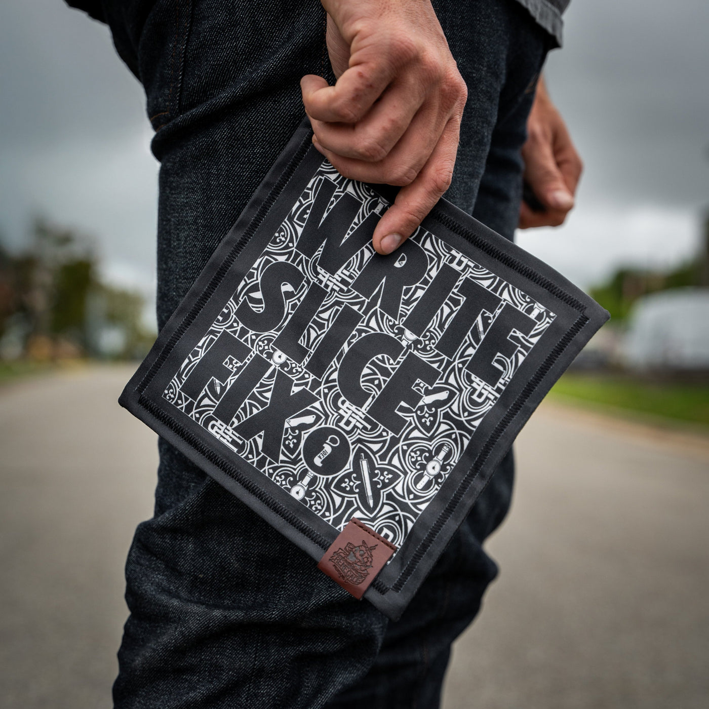 Person holding a black and white Write Slice Fix Hank accessory with bold graphic text outdoors