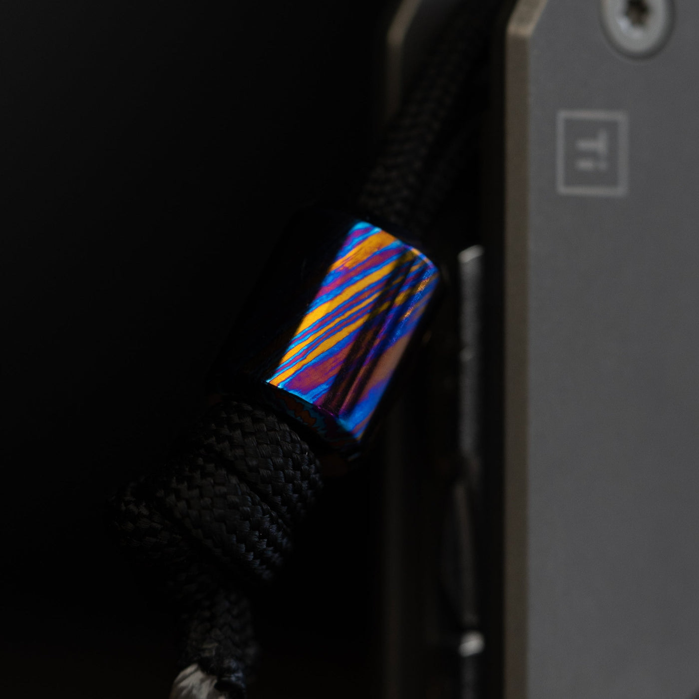 Damascus lanyard bead with vibrant blue and orange patterns attached to black paracord by Big Idea Design LLC