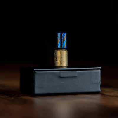 Damascus lanyard bead in blue and gold tones displayed on a black box by Big Idea Design LLC