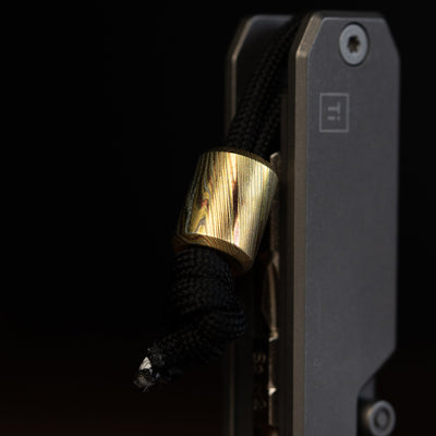 Damascus lanyard bead on black paracord attached to a gray metal tool handle by Big Idea Design LLC