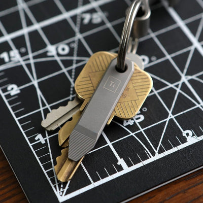 Mini Titanium Pry Bar EDC attached to keyring with multiple keys on a black grid cutting mat