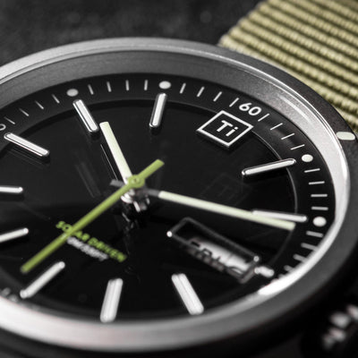 Close-up of Big Idea Design LLC solar titanium field watch with black dial and green fabric strap