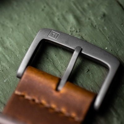 Close-up of solar titanium field watch buckle with brown leather strap by Big Idea Design LLC