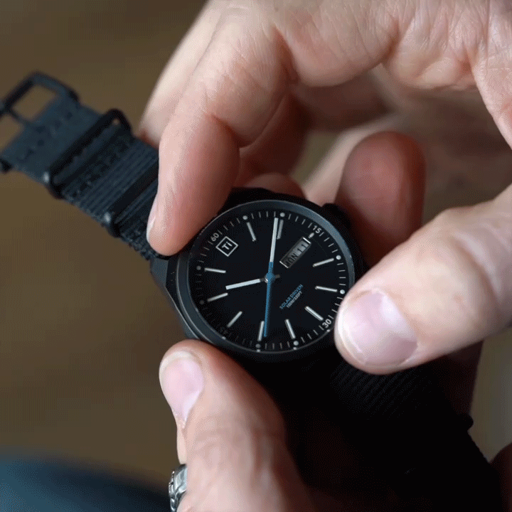 Black solar powered titanium watch with day and date display held in hand by person