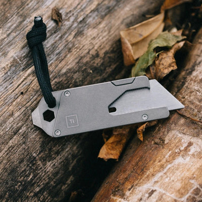 Titanium Pocket Tool EDC with a folding blade and black lanyard on a wooden surface