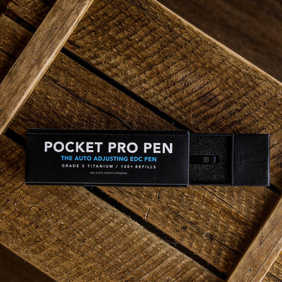 BIG IDEA DESIGN LLC Pocket Pro Pen box on wooden surface showing Pocket Pro pens packaging and titanium EDC pen