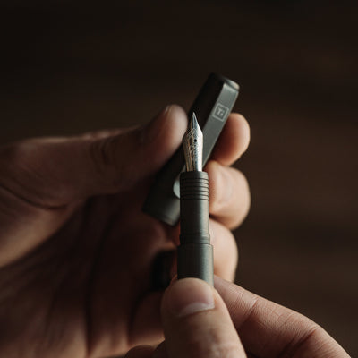 Black fountain pen for EDC enthusiasts with silver nib held by hands by Big Idea Design LLC