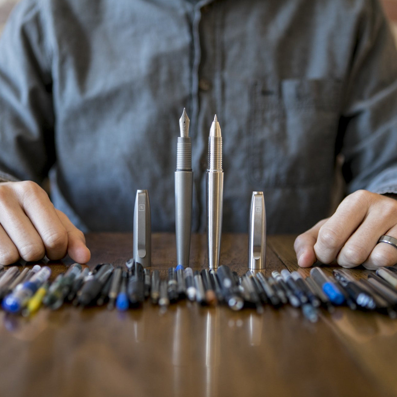 Big Idea Design LLC Titanium Fountain Pen displayed upright with cap beside various pens on wooden table